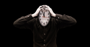 Person in a black shirt holding their head with a large clock replacing their face against a dark background, symbolizing stress, burnout, time pressure, and feeling overwhelmed.