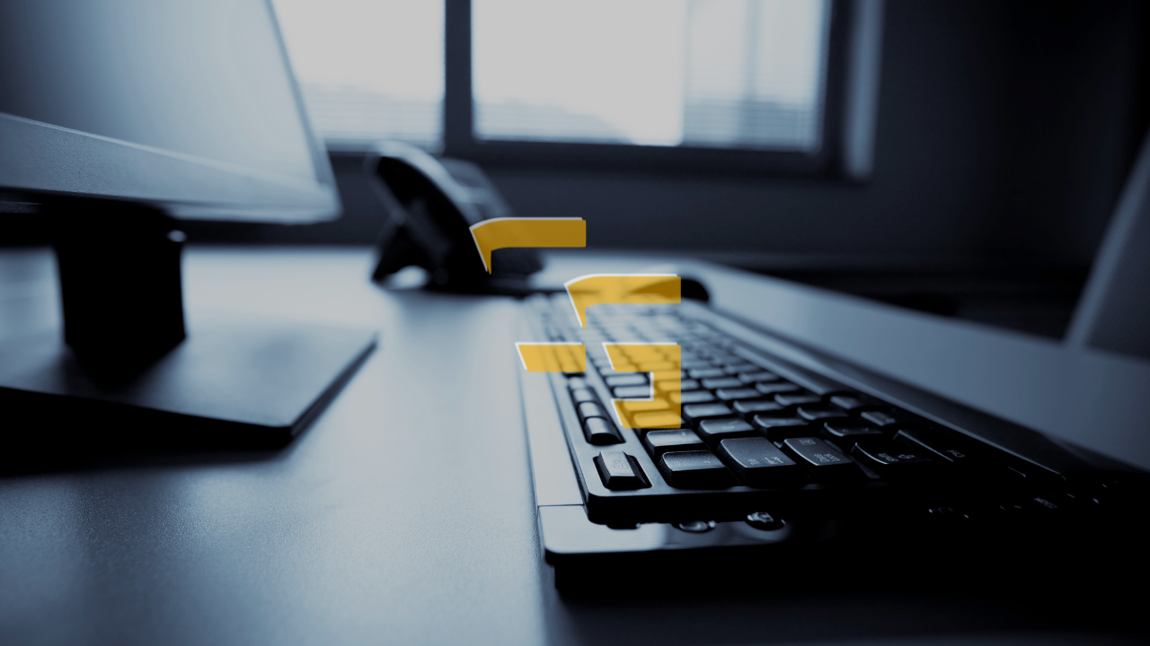 Close-up of a desktop keyboard and office workstation with a monitor in the background, representing work, productivity, or digital business.