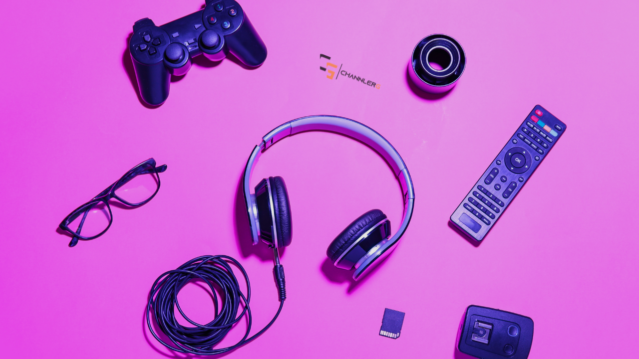 Gaming accessories flat lay including controller, headset, remote, glasses, and cables on a neon pink background.