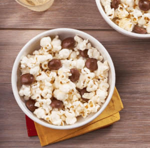 Bowl of buttered popcorn mixed with Milk Duds chocolate candies on a wooden table