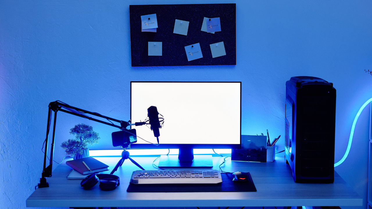 Clean gaming and streaming desk setup with monitor, microphone on boom arm, PC tower, and blue ambient lighting.