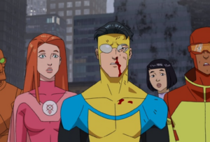 Injured Invincible with blood on his face standing alongside Atom Eve and the Teen Team in a city setting.