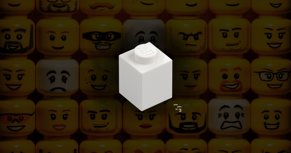 White LEGO brick displayed in front of a colorful wall of LEGO minifigure faces, representing gift ideas for adult LEGO fans.