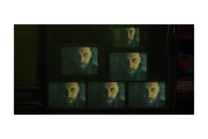 Alan Wake 2 scene showing a man’s face displayed across multiple television screens in a dark room