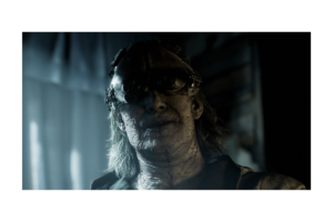 Disturbing character wearing mechanical goggles in a dark scene from Resident Evil Requiem